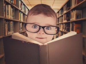 36536917 - a cute little baby is wearing eye glasses and reading a library book for an education or learning concept.